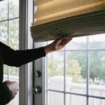 Woman Adjusts Roman Shade on French Door