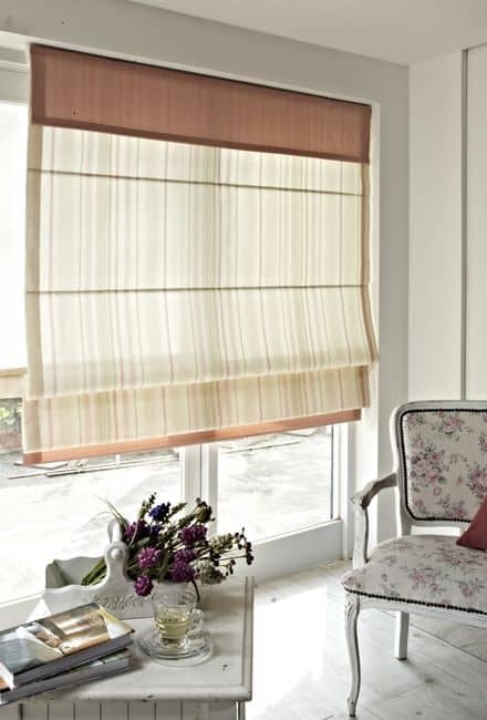A Roman shade on a bright window above a small table with flowers