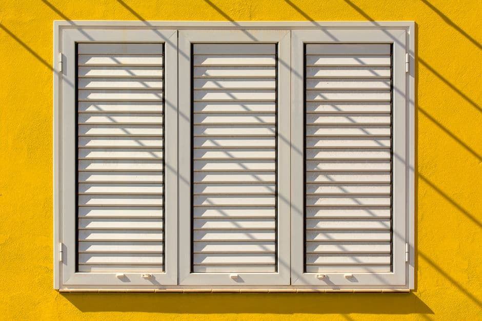 White louvered shutters on a yellow wall