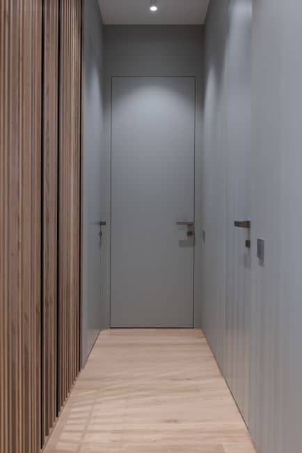 A narrow bright hallway with gray doors close to the walls