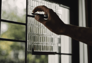 An image showcasing a close-up of hands holding a glass scraper at a slight angle, effortlessly gliding it across the surface of a French door, effectively removing the grids