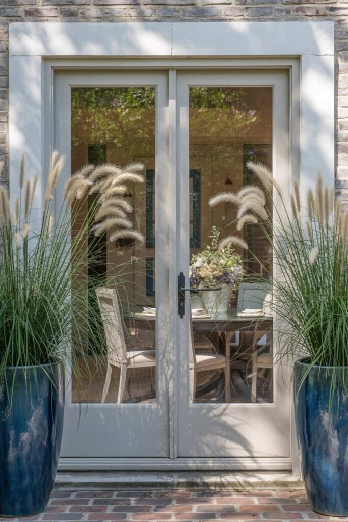 French patio door flanked by matching tall ceramic planters containing ornamental grasses