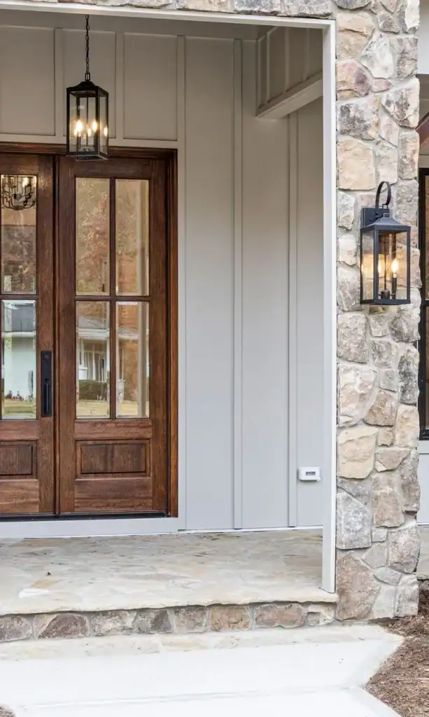 Black wall lanterns on each side of a wood French front door with a matching pendant lantern hanging in the covered entry.